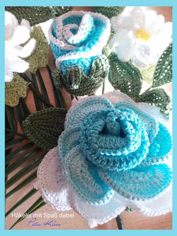 Detailansicht gehäkelter Blüten und Blätter in Blau, Weiß und Grün