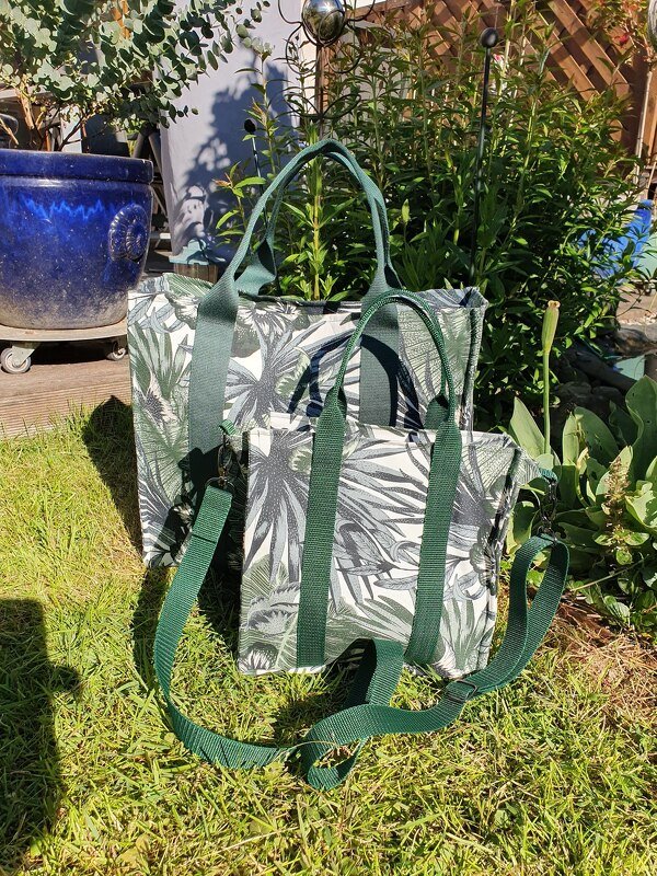 Zwei grüne Stofftaschen mit Blattmuster und dunkelgrünen Tragegurten auf Gras