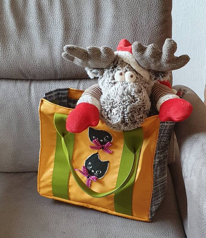 Gelbe Stofftasche mit grünen Henkeln und schwarzen Katzen-Applikationen, innen ein Kuscheltier mit Geweih