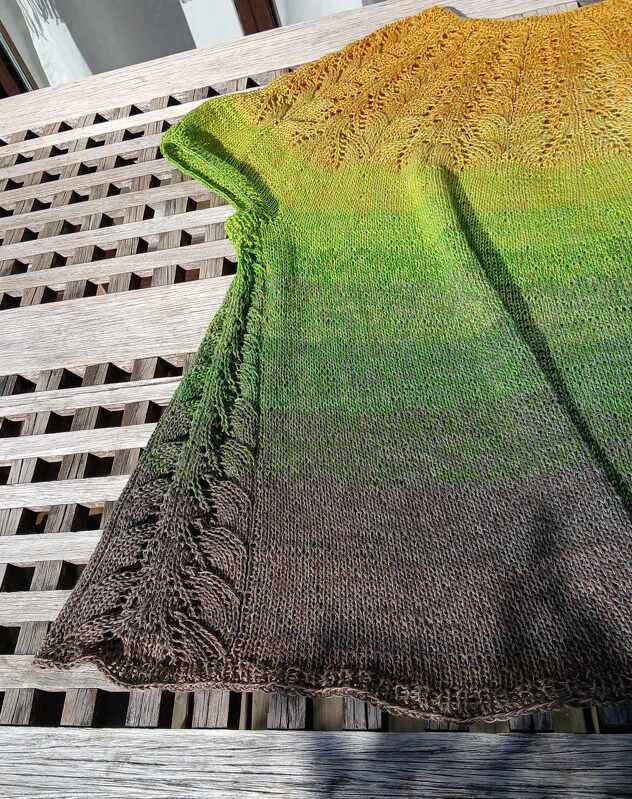 Gestrickte Damen-Tunika in Ombré-Farben mit Ajour- und Blattmustern auf einer Holzbank