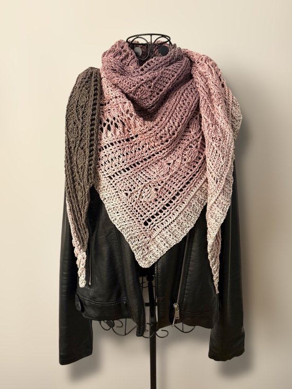 Crocheted triangle shawl with gradient colors from dark taupe to pale pink, draped on a mannequin over a black jacket.