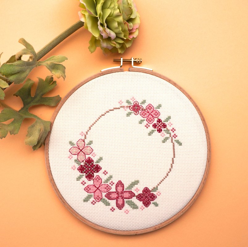 Holzstickrahmen mit rundem Kreuzstich-Blumenkranz in Rosa und Rot auf weißem Stoff