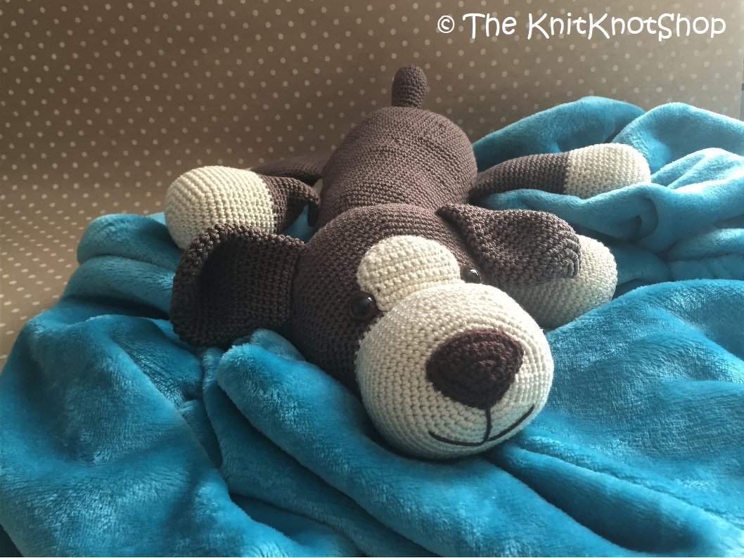 Gehäkelter Amigurumi-Hund in Braun und Creme auf türkisfarbener Decke
