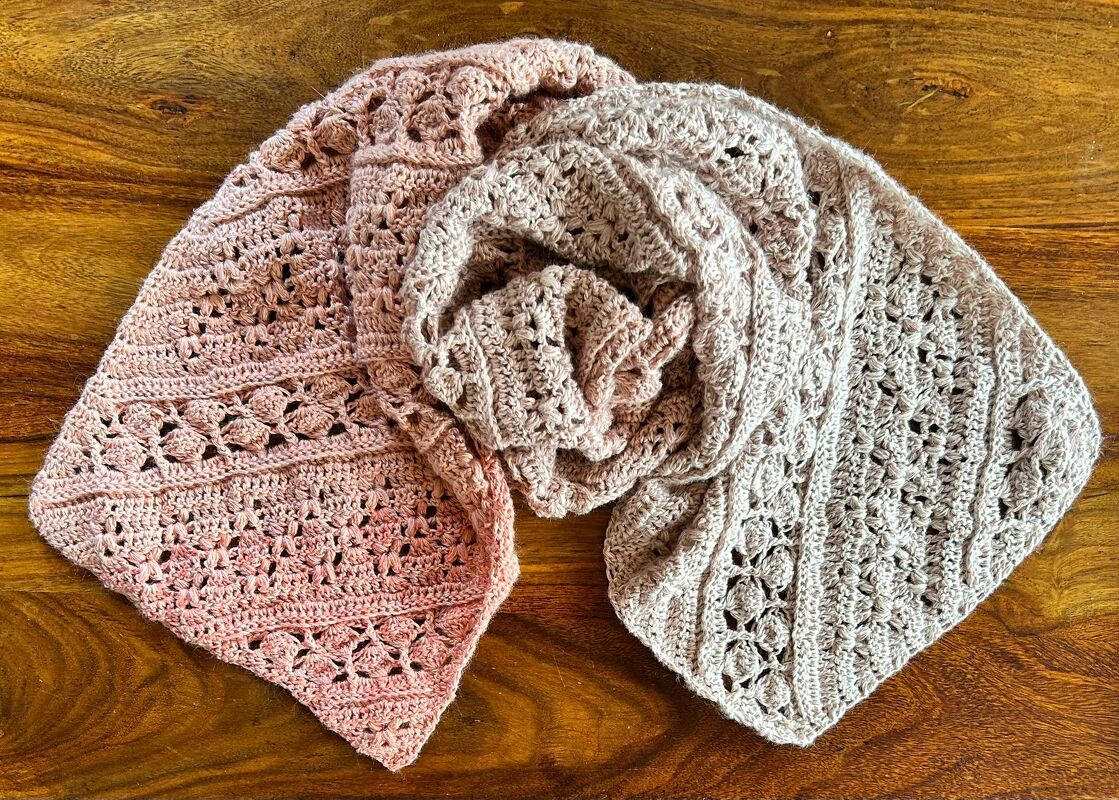 Feiner gehäkelter Schal in Rosé und Beige mit offenen Lochmustern, drapiert auf Holz.