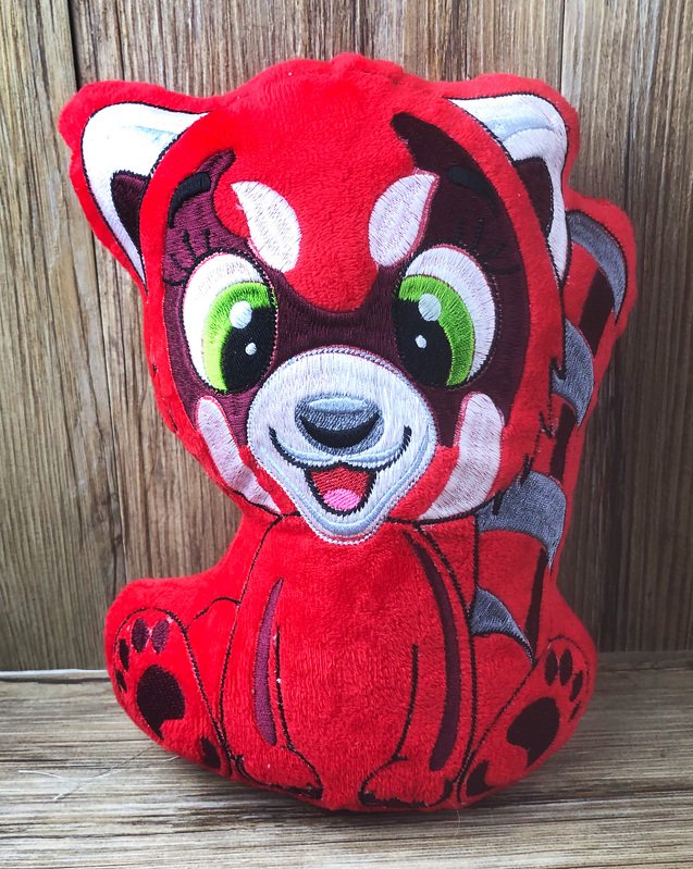 Gestickter roter Panda in Plüschtierform mit grünen Augen vor rustikalem Holz.