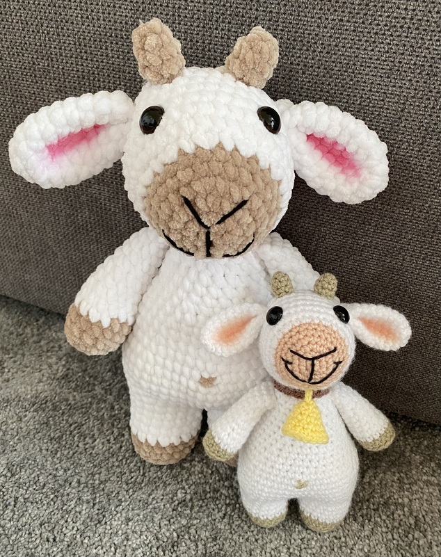 Großes und kleines weiß‑braunes Amigurumi‑Schaf nebeneinander, kleines Schaf mit gelbem Glöckchen