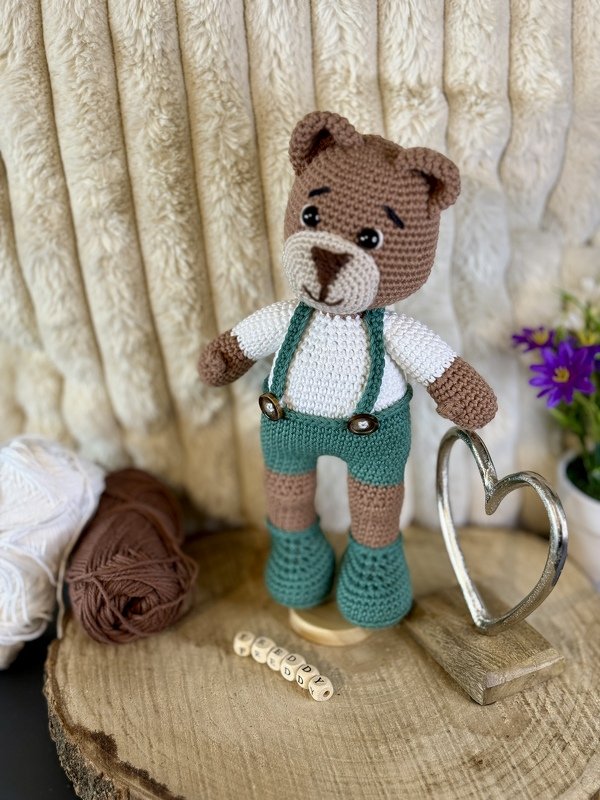Nahaufnahme gehäkelter Teddybär mit grünen Hosenträgern und Wollknäueln