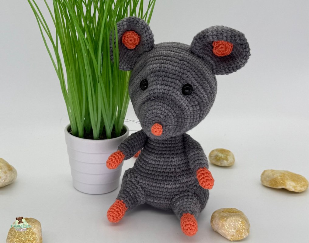 Gehäkelte graue Amigurumi-Maus mit orangefarbenen Akzenten und schwarzen Augen, sitzend