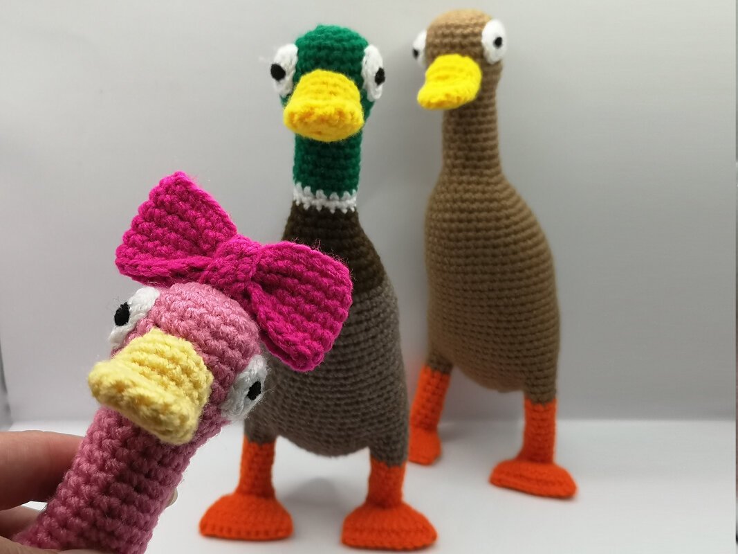 Three crocheted amigurumi ducks on white background; pink duck with bow in front