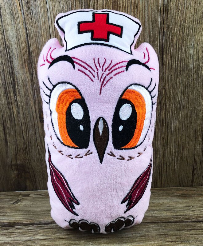 Rosa bestickte Plüscheule mit Krankenschwesterhaube und rotem Kreuz vor Holzhintergrund