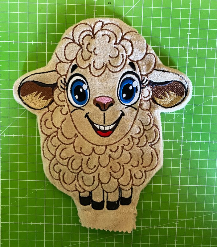 Besticktes Schaf mit großen blauen Augen und breitem Lächeln auf einer grünen Schneidematte