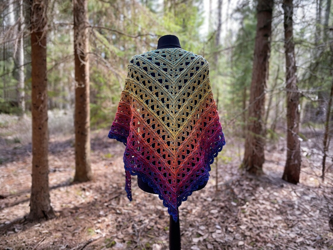 Multicolor crocheted triangle shawl with openwork lace draped on a mannequin in a forest