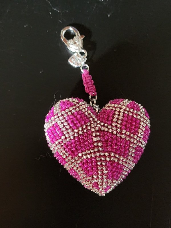 Gehäkelter herzförmiger Schlüsselanhänger in Fuchsia mit silberfarbenen Perlen und Karabiner auf dunklem Hintergrund