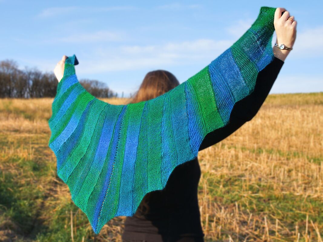 Person holding a blue and green striped crescent shawl, seen from behind.