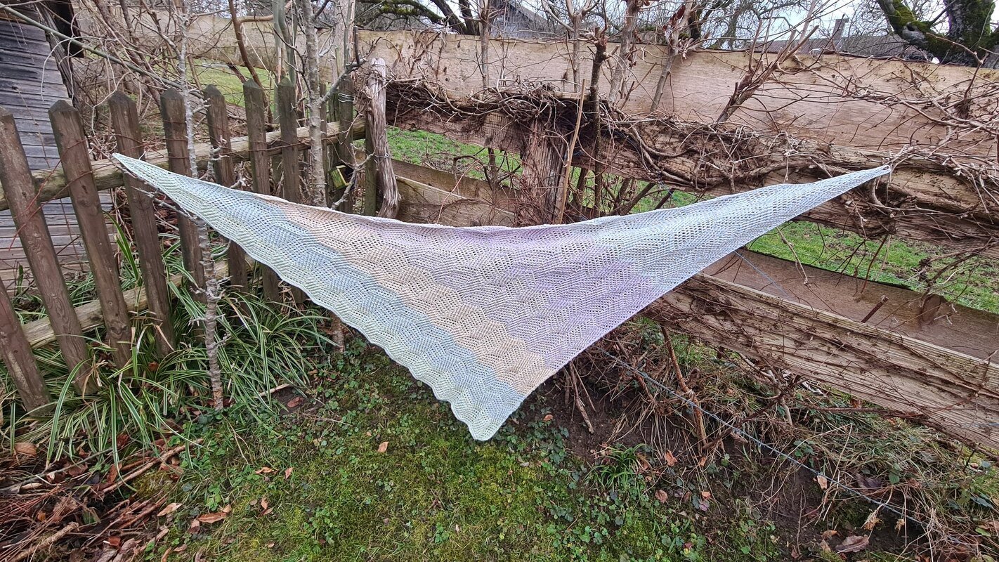 Crocheted triangle shawl with ombre colors and hexagon stitch, draped on a wooden fence.