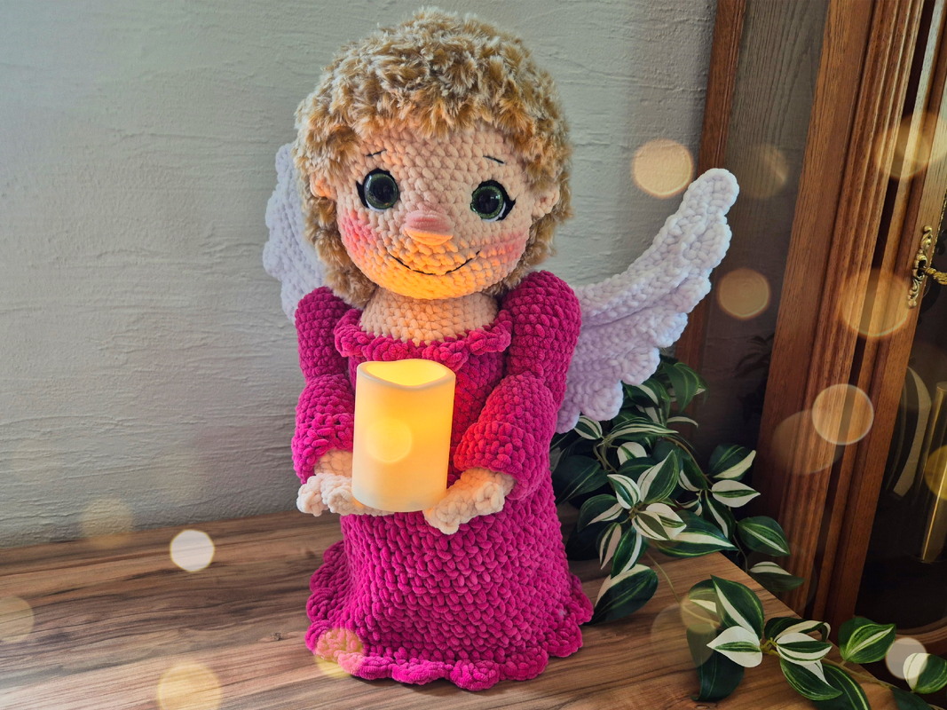 Amigurumi-Engel mit weißen Flügeln, rosa Kleid und leuchtender Kerze als Detailansicht