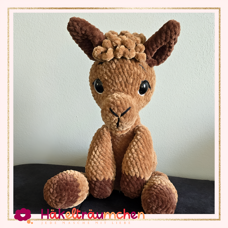 Gehäkeltes braunes Lama Amigurumi mit dunklen Ohren und Pfoten, sitzend.