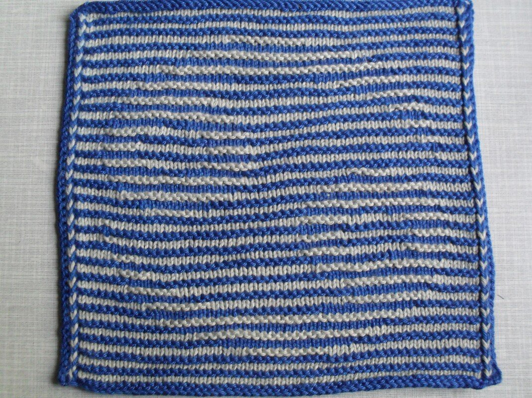 Gestricktes Rechteck in Blau und Weiß mit leicht gewellten horizontalen Streifen und blauer Umrandung.