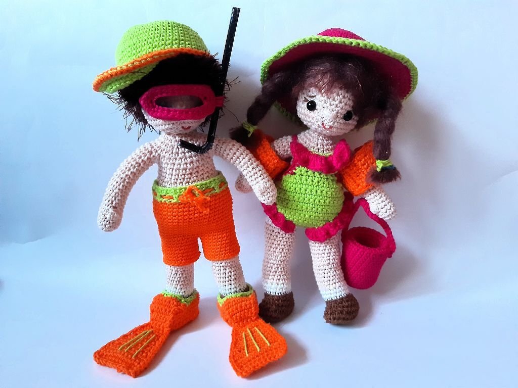 Zwei gehäkelte Amigurumi-Puppen: links mit Hut, Schnorchelbrille und orangefarbenen Flossen, rechts mit Hut, grün-pinkem Outfit und kleinem Eimer