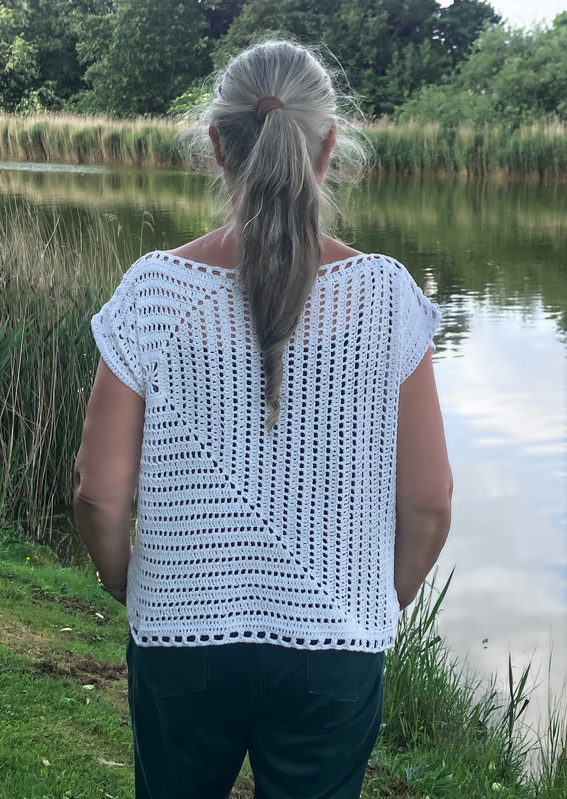 Rückenansicht einer Frau am See, trägt weißes gehäkeltes Top mit diagonalem Muster und kurzen Ärmeln