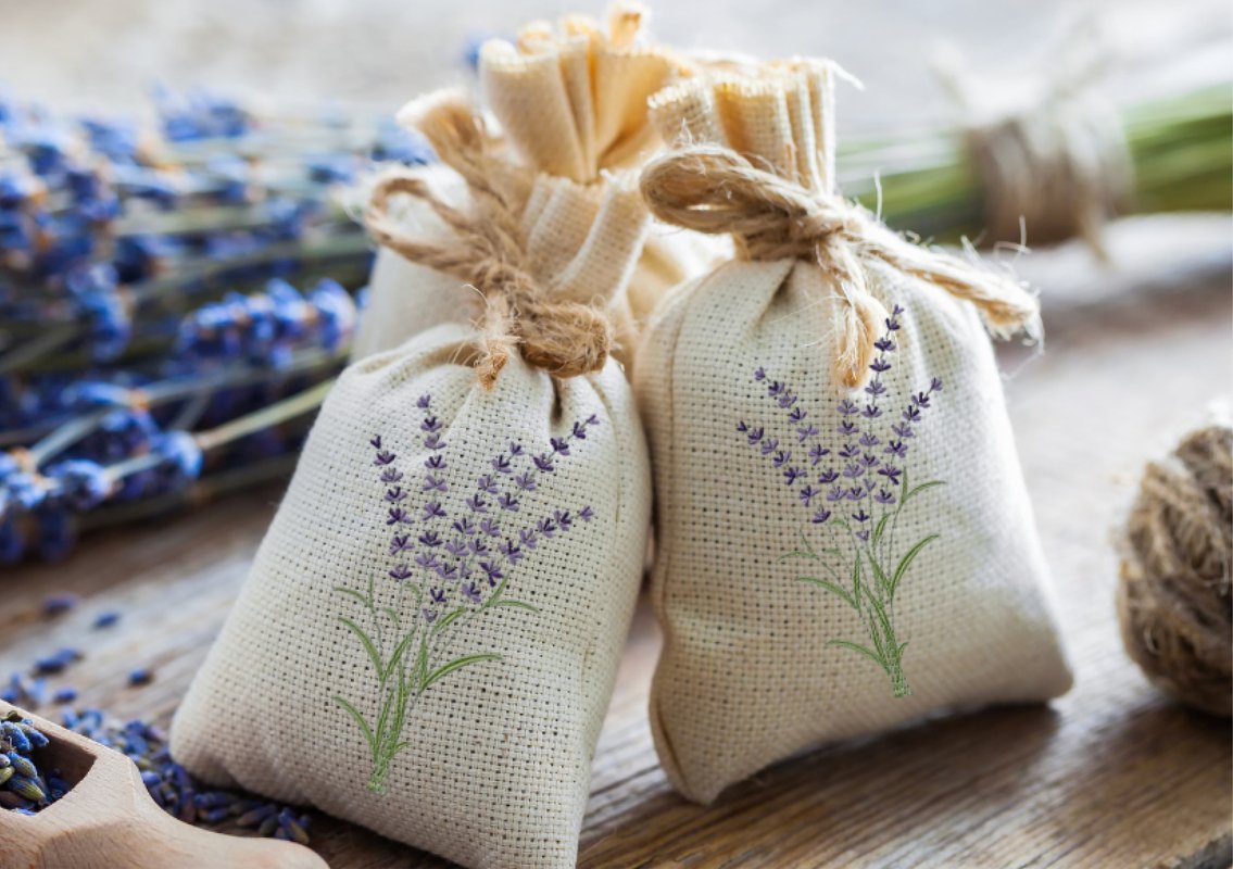 Zwei bestickte Stoffbeutel mit Lavendelmotiv, getrockneter Lavendel und Holzlöffel auf Holzoberfläche