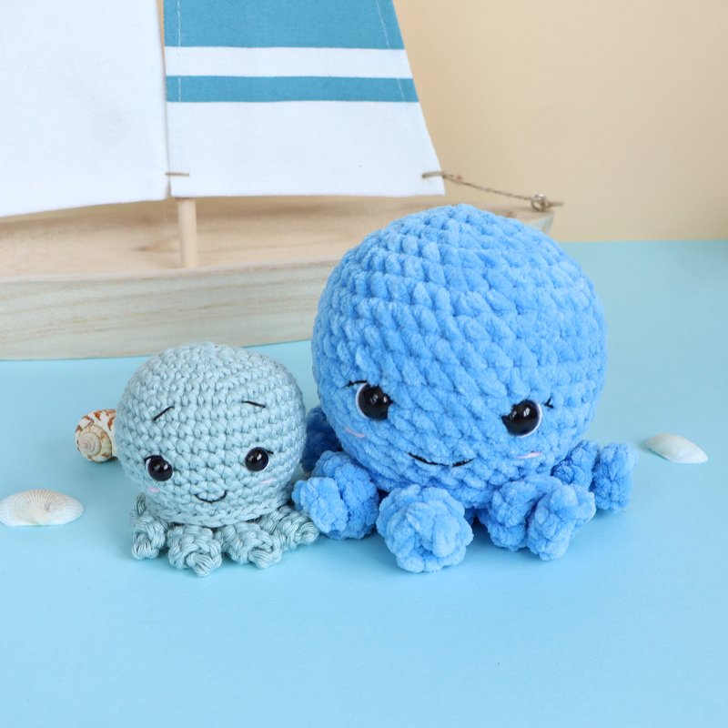 Großer blauer und kleiner mintfarbener gehäkelter Oktopus nebeneinander auf blauem Hintergrund