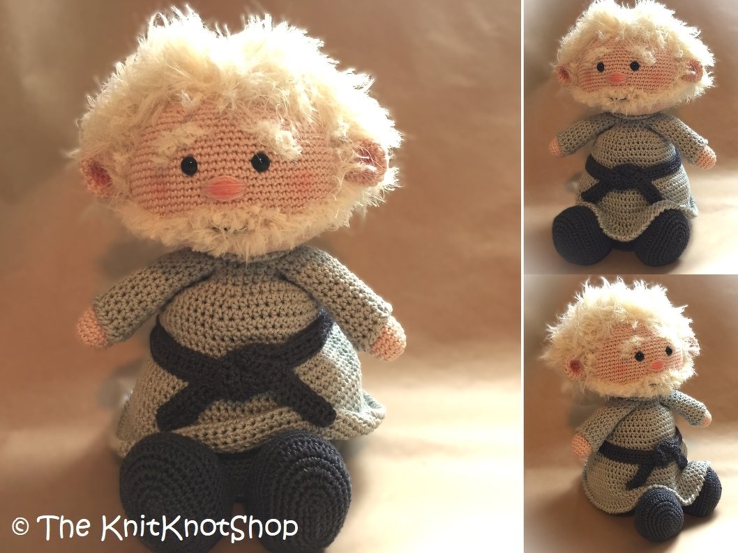 Whimsical crocheted gnome amigurumi with fluffy white hair and beard, pink cheeks, blue-gray tunic and dark sash.