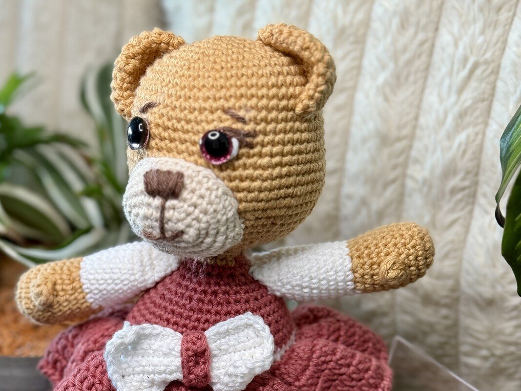 Gehäkelter Amigurumi-Teddybär in hellbraun mit rosa Kleid und weißer Schleife