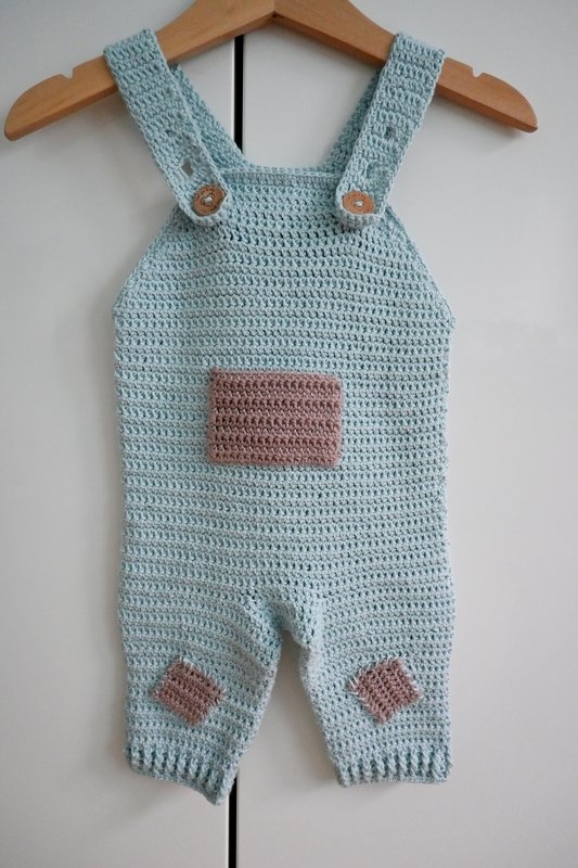 Gehäkelter pastellmintfarbener Baby‑Strampler mit altrosa Tasche und Holzknöpfen an einem Bügel