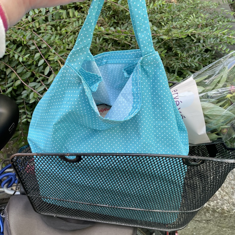 Fröhliche türkis-weiße gepunktete Stofftasche mit kurzen Henkeln und hellem Innenfutter im Fahrradkorb mit Blumen