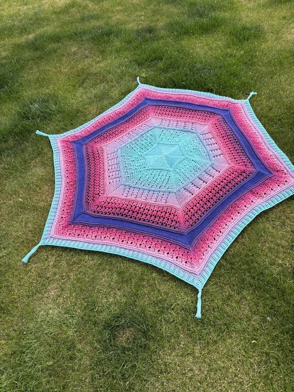 Sechseckige gehäkelte Decke in Türkis, Rosa und Lila mit Quasten, auf Gras liegend