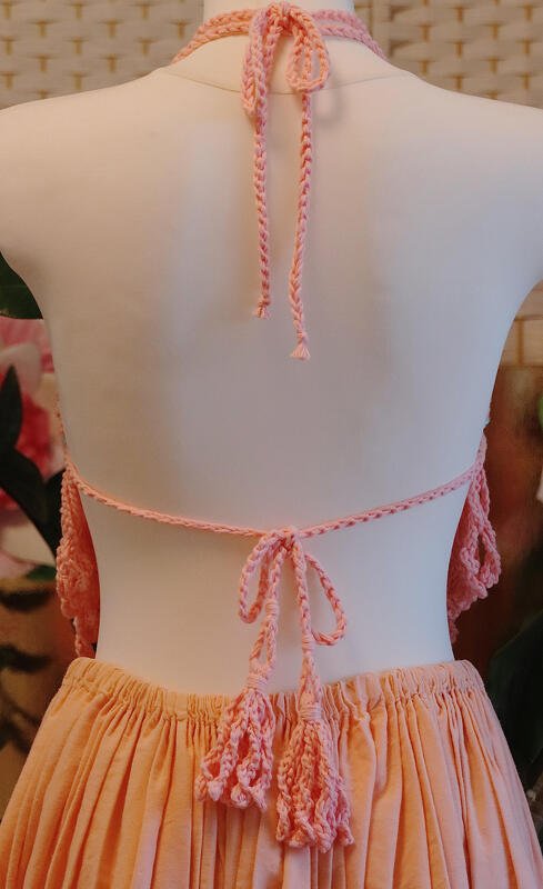 Rückenansicht eines rosafarbenen Häkeltops mit geflochtenen Nacken- und Rückenbändern und Quasten auf einer Schneiderpuppe.