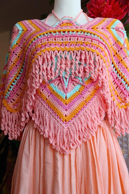 Gehäkelter Poncho in Rosa, Orange und Hellblau mit Fransen und V‑Muster auf einer Schaufensterpuppe