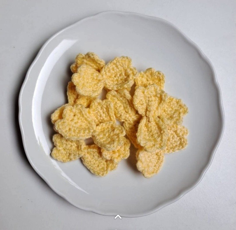 Mehrere gelbe, gehäkelte Schleifen auf weißem Teller, ähnlich Farfalle