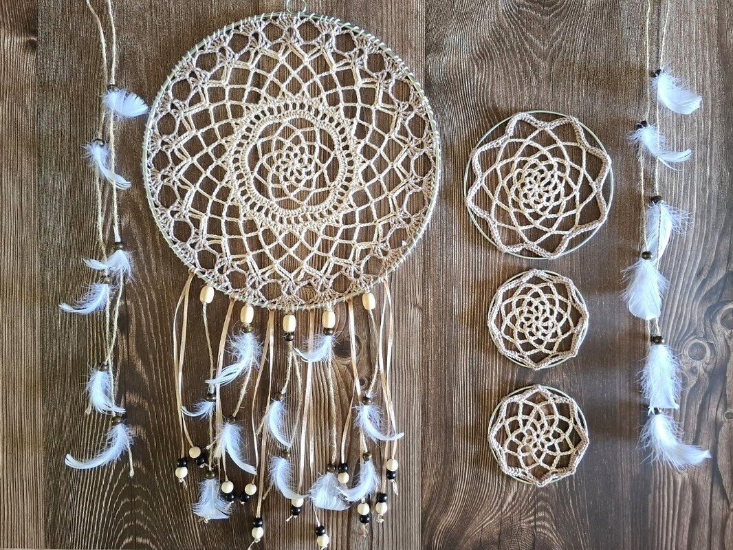 Beiger gehäkelter Traumfänger mit Holzperlen und weißen Federn neben drei kleinen gehäkelten Mandalas auf Holzhintergrund
