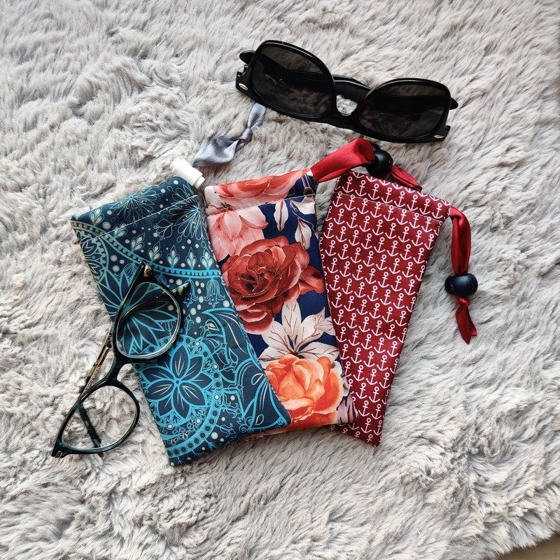 Drei gemusterte Stoff-Brillenetuis mit Kordelzug und zwei Brillen auf flauschigem Untergrund