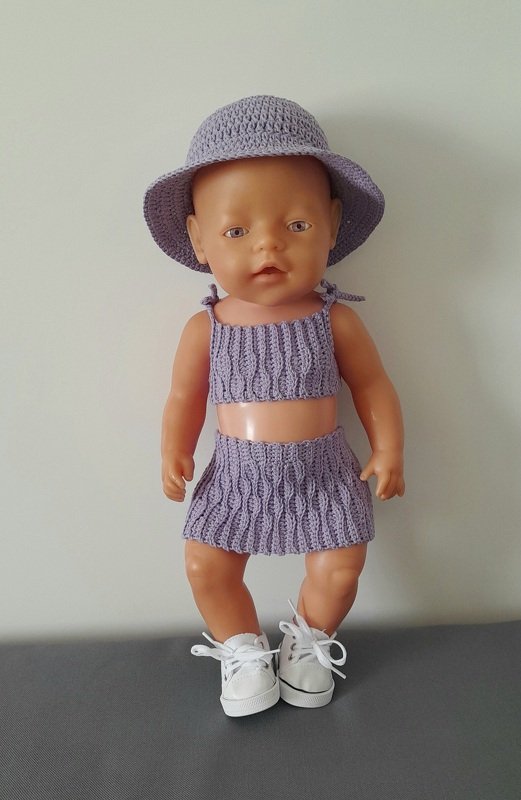 Puppe trägt ein gehäkeltes lilafarbenes Outfit bestehend aus Top, Rock und Hut.