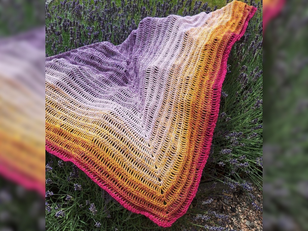Gehäkeltes Dreieckstuch mit Verlaufsgarn in Lila, Orange und Gelb mit pinker Kante auf Lavendel