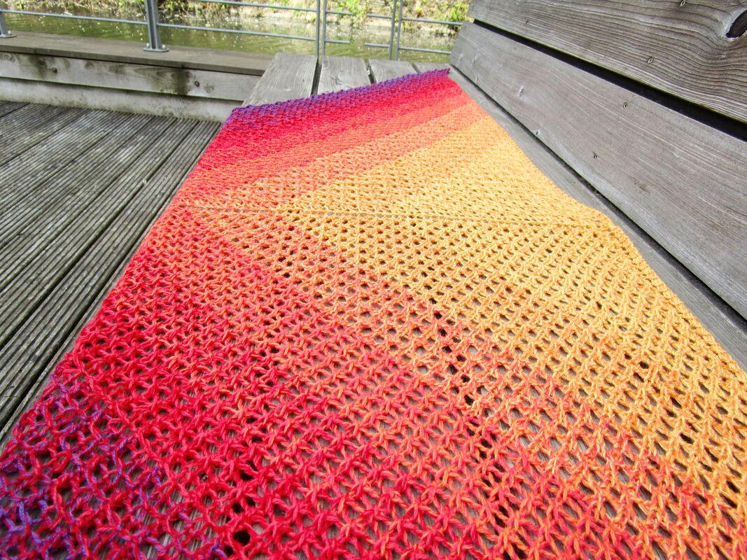Triangle ombr
shawl in red to yellow gradient draped flat on a wooden bench showing lace texture.