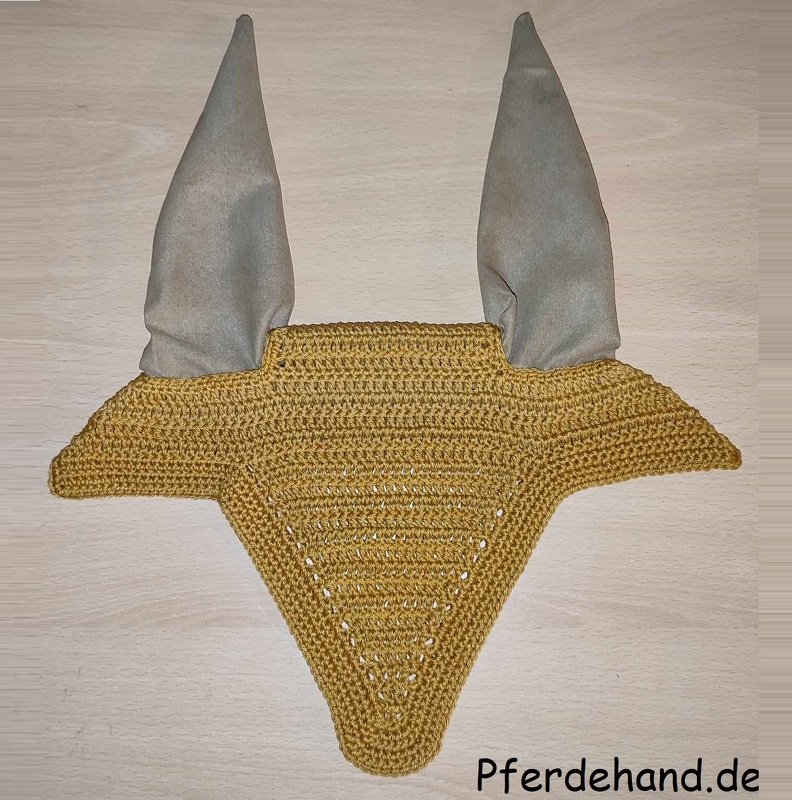 Gehäkelte senfgelbe Fliegenhaube mit hellgrauen Ohrenschutz-Bezügen, flach auf hellem Untergrund fotografiert.
