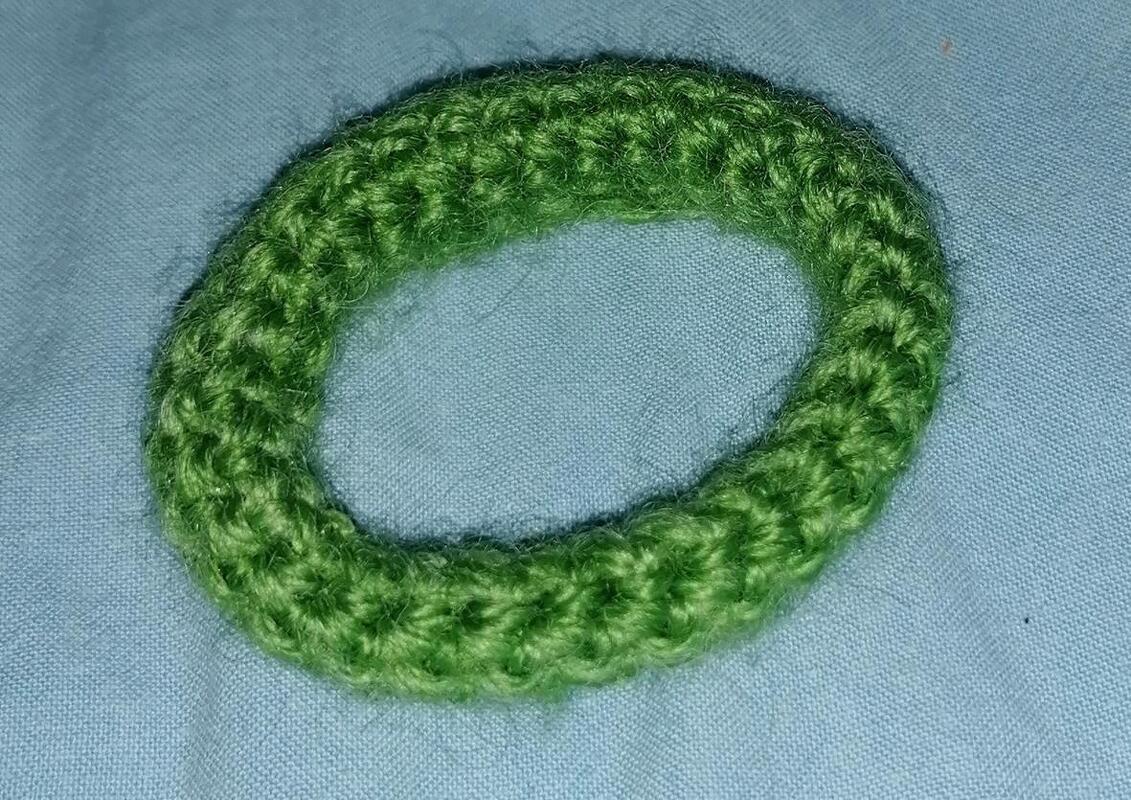 Ovaler grüner gehäkelter Ring aus Garn auf hellblauem Stoff