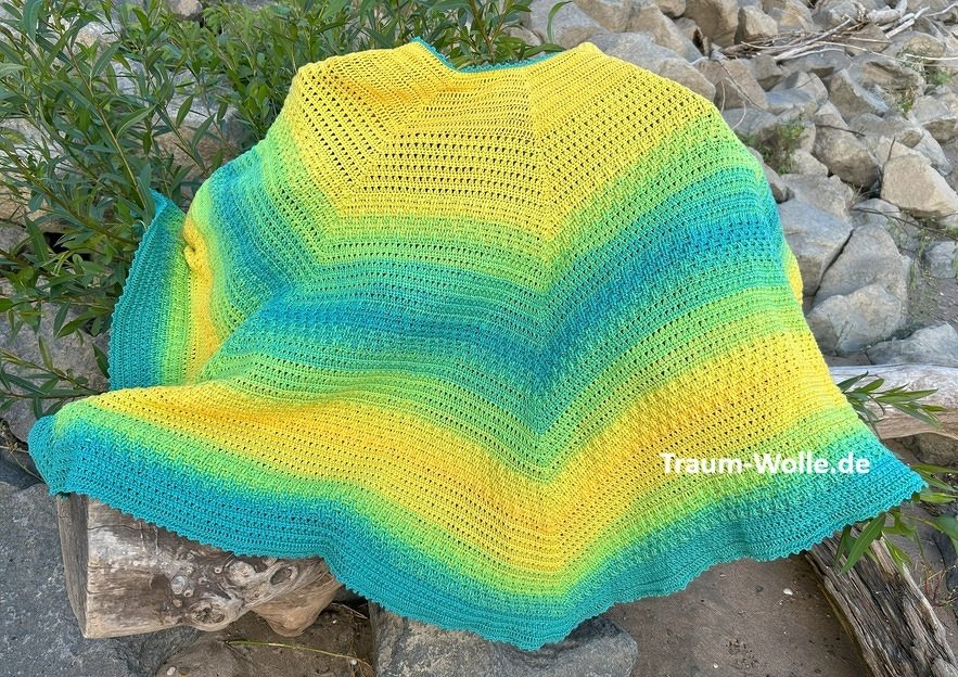 Gehäkelter Damenponcho in Gelb, Grün und Blau auf steinigem Untergrund