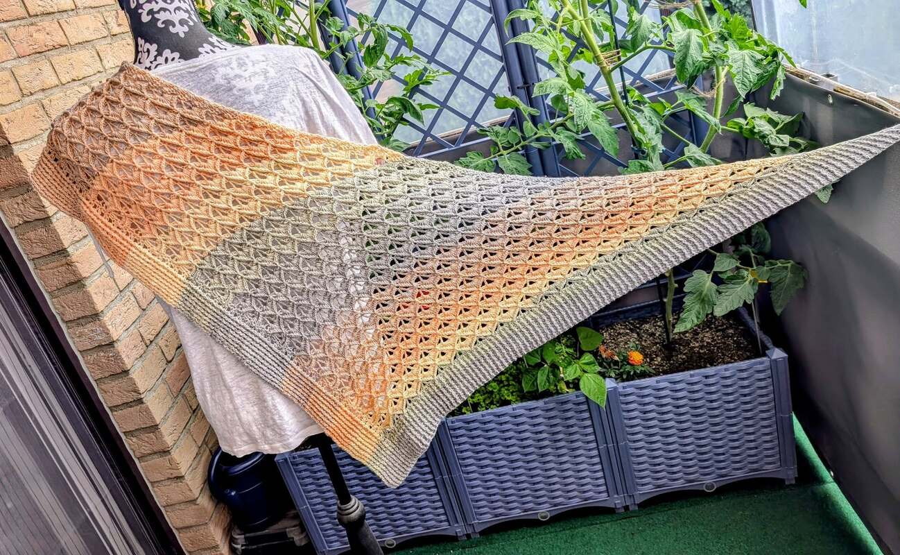 Crocheted triangle shawl in beige-to-peach-to-grey gradient draped over a chair on a balcony