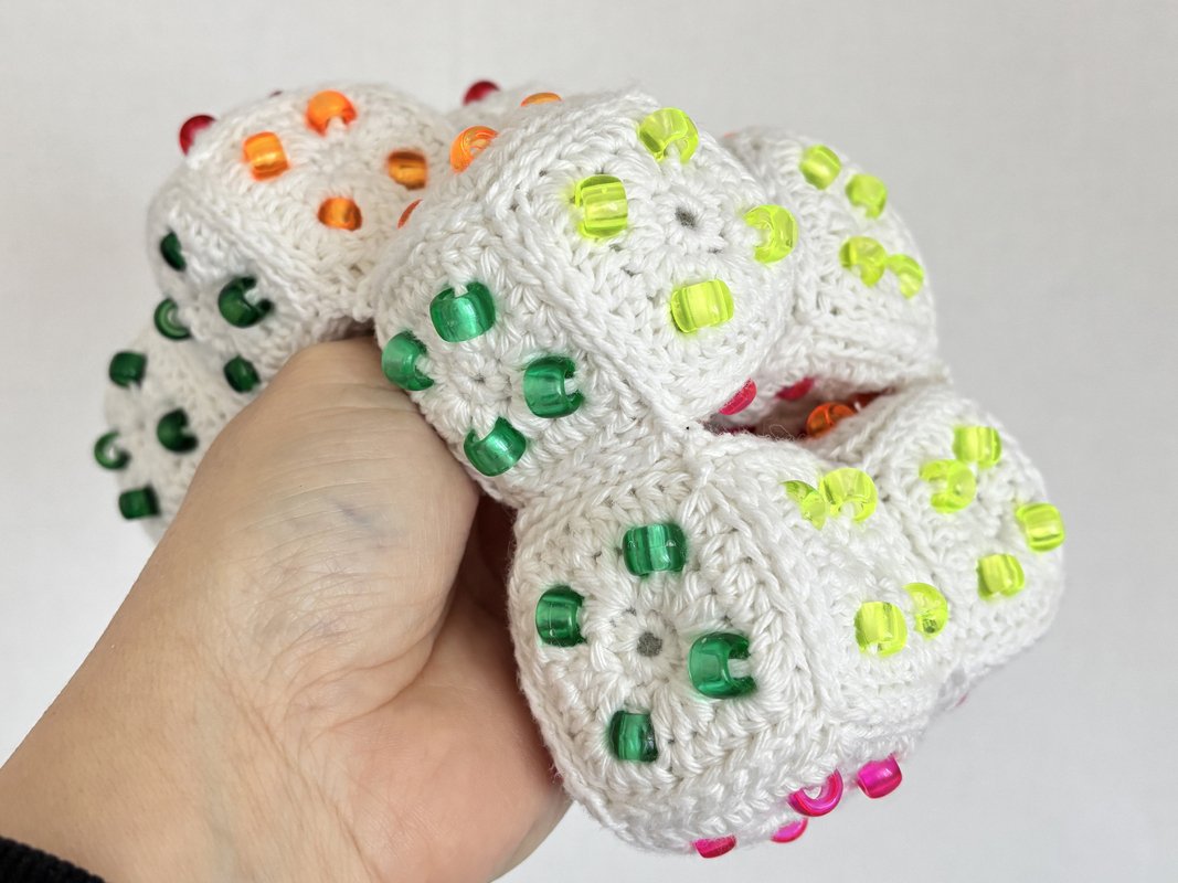 Hand holding a white crocheted ball of joined motifs decorated with translucent green, yellow, orange and pink beads