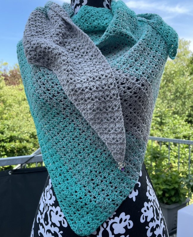 Gehäkeltes Dreieckstuch auf einer Schneiderpuppe mit Farbverlauf von Grau zu Türkis und offenem Häkelmuster