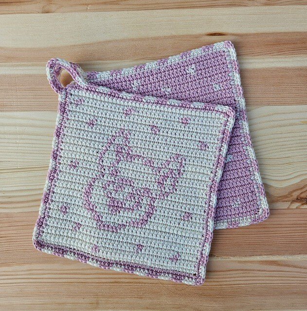 Zwei quadratische, gehäkelte Topflappen in Rosa und Creme, einer mit Hasenmotiv und Aufhängeschlaufe