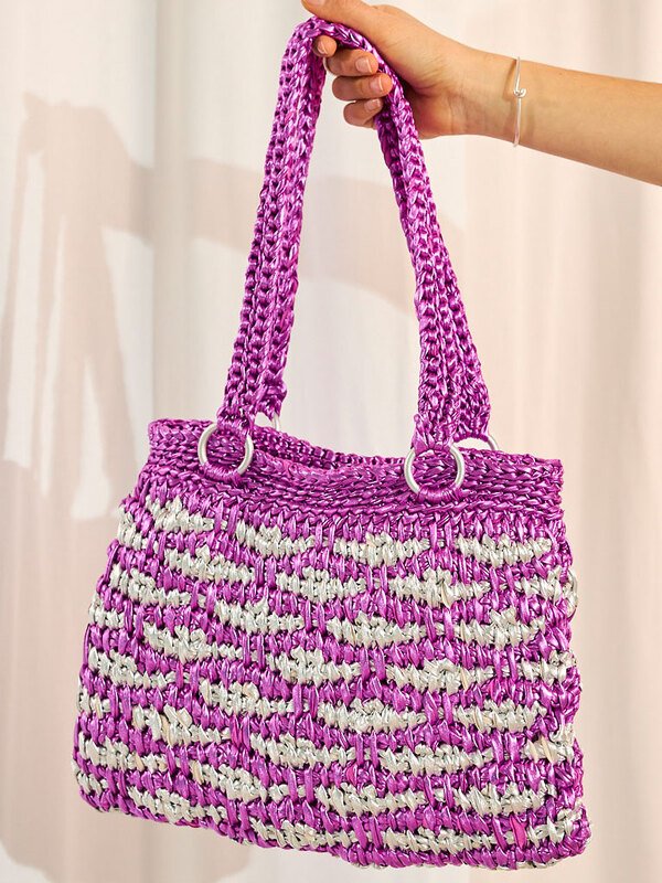 Hand hält eine violett-silberne Henkeltasche mit dichtem Häkelmuster.