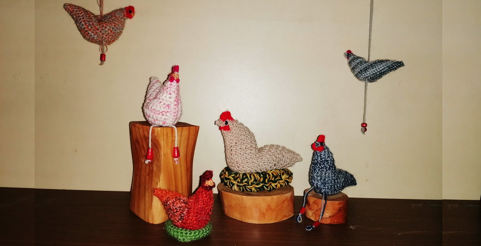 Gehäkelte Amigurumi‑Hühner in Pastell- und Erdtönen auf Holzpodesten und hängend