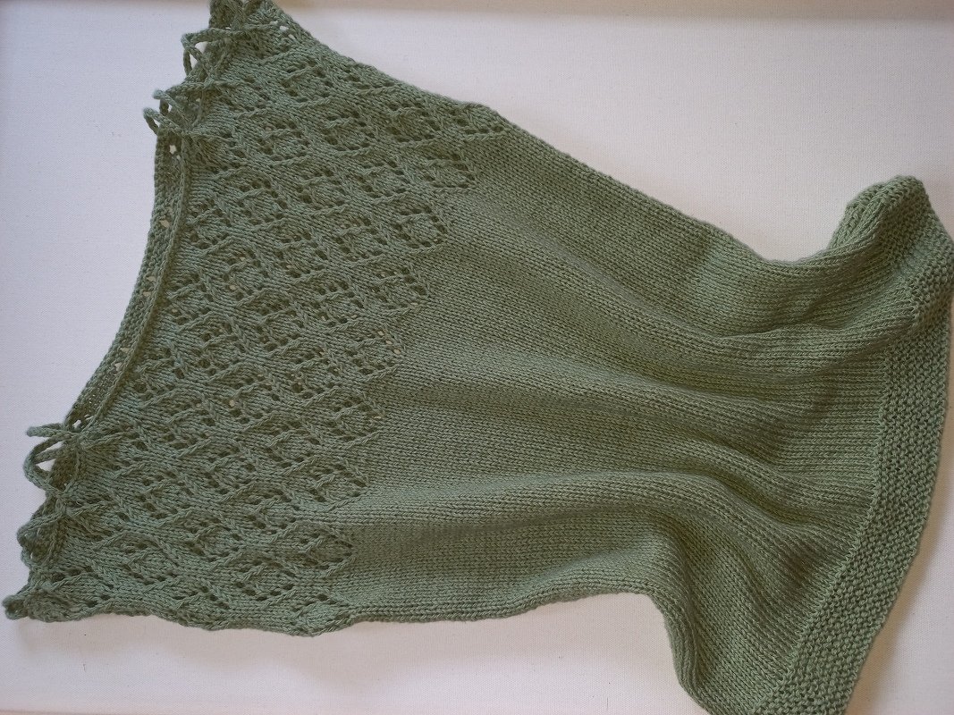 Salbeigrünes gestricktes Damen-Top mit Ajourmuster oben und glatt rechts gestricktem Unterteil auf hellem Hintergrund.