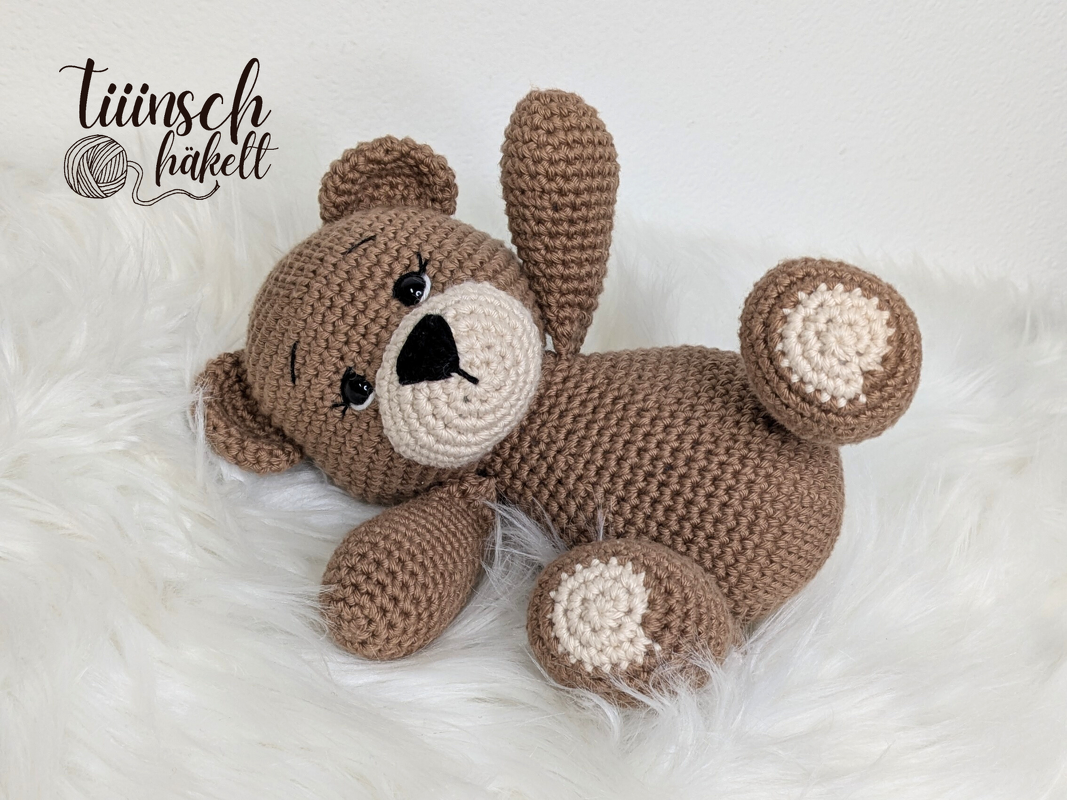 Brauner gehäkelter Teddybär mit beiger Schnauze auf weißem Fell